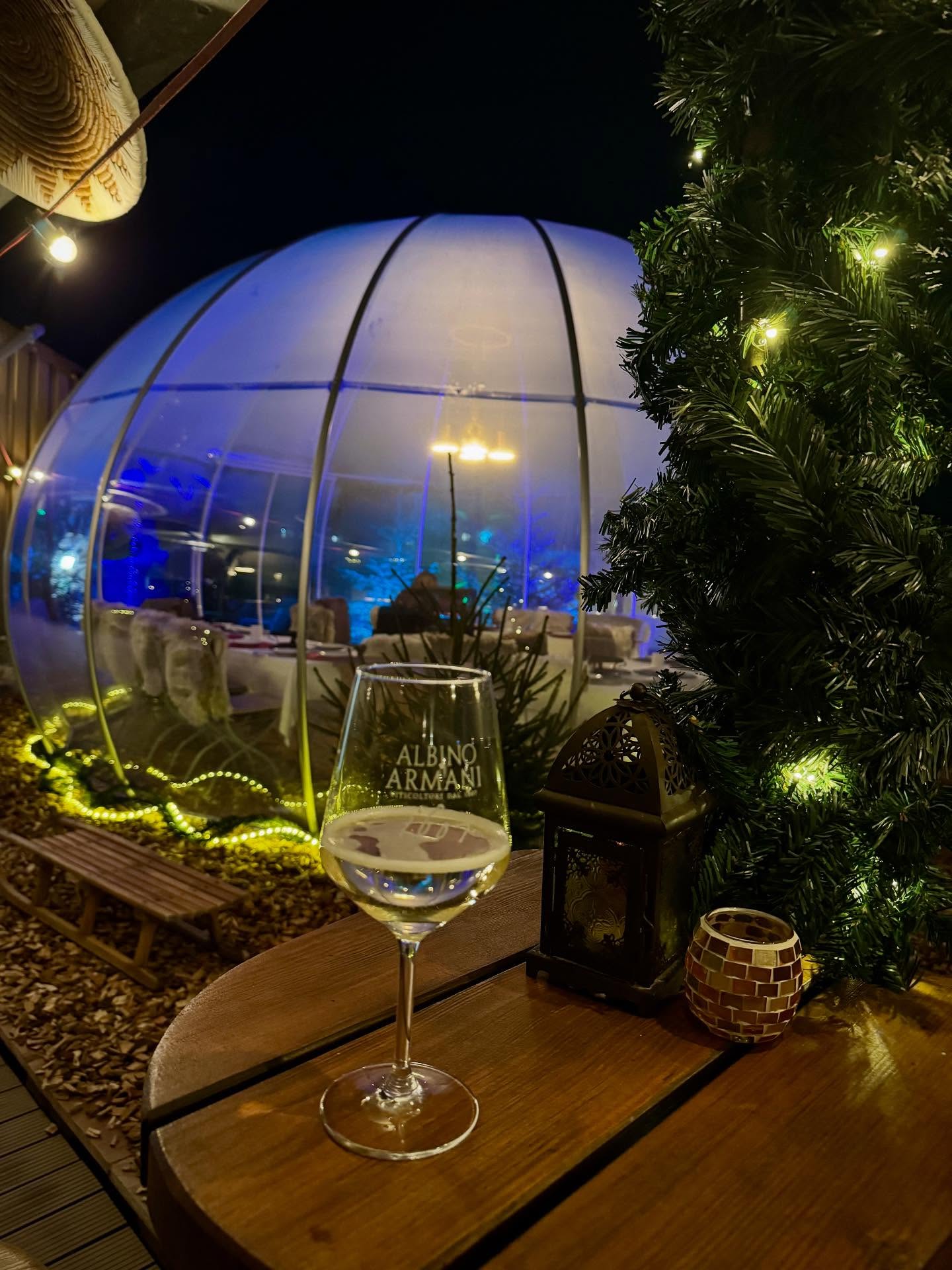 Weissweinglas und Laterne auf dem Holztisch vor dem blau beleuchteten Fondue-Iglu in Aarau