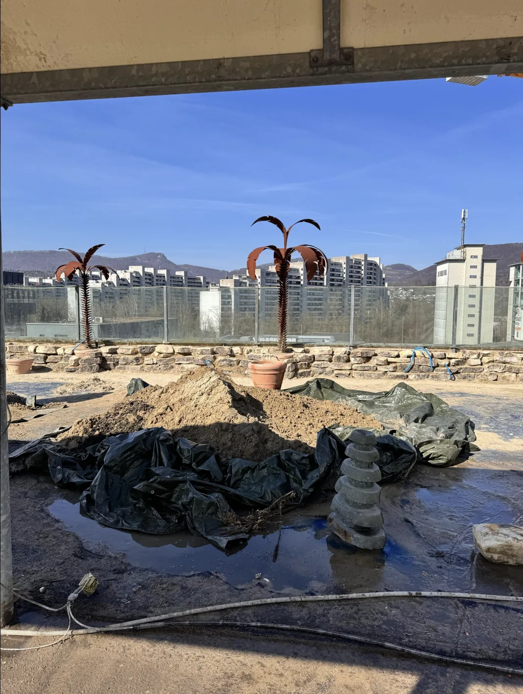 Steinmauer mit Metallpalmen und Erdhaufen vor der Fertigstellung